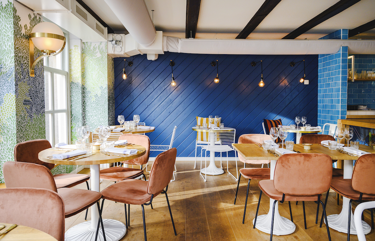 Dining area at Brasserie Ultimo with terracotta velvet chairs and a deep-blue feature wall