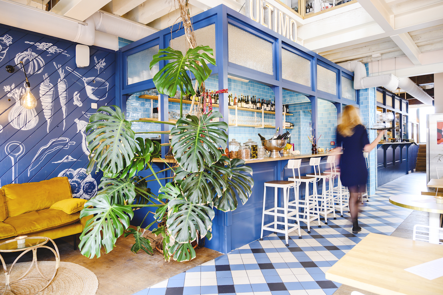 The Ultimo bar with house plants, white-tile floor, and the Ultimo wordmark above the back bar